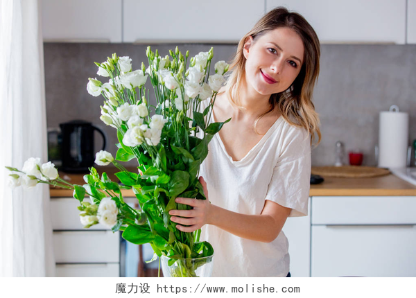 一个穿着白色短袖在把花朵插进花瓶里的女人女孩在把白玫瑰放进花瓶之前, 准备一束白玫瑰